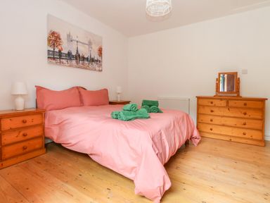 A bedroom with a double bed with pink bedding and green towels on top two wooden bedside tables with white lamps a wooden dresser with a mirror and a painting above the bed at Coldharbour Farm Bungalow Annexe Coldharbour near Wareham