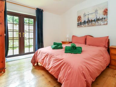 A bedroom with a double bed covered in pink bedding with green towels on top next to wooden bedside tables with lamps and a large window with dark curtains at Coldharbour Farm Bungalow Annexe Coldharbour near Wareham