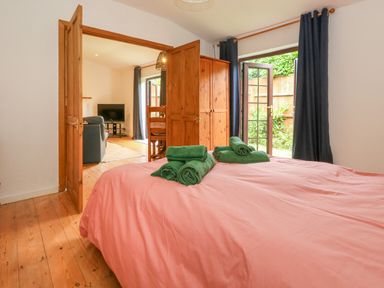 A bedroom with a bed with green towels on it a wooden wardrobe and an open door leading to a living room at Coldharbour Farm Bungalow Annexe Coldharbour near Wareham