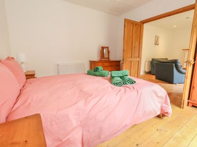 A bedroom with a pink bedspread green towels on the bed wooden furniture and an adjoining room with blue armchairs at Coldharbour Farm Bungalow Annexe Coldharbour near Wareham