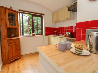A kitchen with wooden cabinets red tiled backsplash a wooden corner cabinet and a countertop with two mugs a plate with a pastry and a toaster at Coldharbour Farm Bungalow Annexe Coldharbour near Wareham