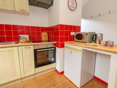 A kitchen corner with wooden cabinets a built-in oven red tiled backsplash a small fridge a microwave electric kettle two mugs and a loaf of bread on the counter at Coldharbour Farm Bungalow Annexe Coldharbour near Wareham