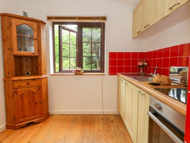 A kitchen with wooden floor cupboards and a corner cabinet with a window showing greenery at Coldharbour Farm Bungalow Annexe Coldharbour near Wareham
