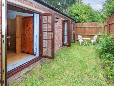 A garden with grass a wooden fence and white metal table and chairs outside a brick building with open glass doors at Coldharbour Farm Bungalow Annexe Coldharbour near Wareham