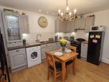 A kitchen with grey cabinets a wooden table set for two a washing machine a black refrigerator and a stove at The Old Sorting Office in Hawarden