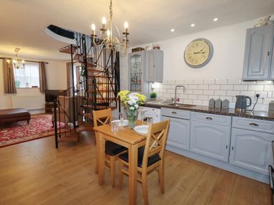 A kitchen and dining area with a wooden table and chairs and a spiral staircase in the background at The Old Sorting Office in Hawarden