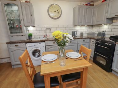 A kitchen with a wooden dining table set for two with flowers in a vase and grey cabinets at The Old Sorting Office in Hawarden