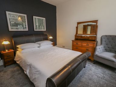 A bedroom with a bed bedside tables lamps a wooden dresser with mirror and a gray armchair at The Old Sorting Office in Hawarden