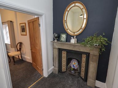 A room with a fireplace decorated with a mirror a globe a picture sculpture and a plant and a chair in an adjacent room at The Old Sorting Office in Hawarden