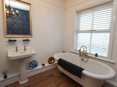 A bathroom with a freestanding bathtub and a pedestal sink below a mirror at The Old Sorting Office in Hawarden