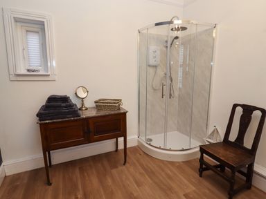 A bathroom with a glass corner shower wooden cabinet with towels and a chair at The Old Sorting Office in Hawarden
