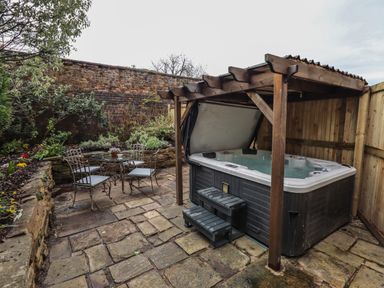 An outdoor area with a hot tub under a wooden pergola and a metal table with four chairs at The Old Sorting Office in Hawarden