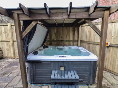 A hot tub with water under a wooden pergola on a stone patio at The Old Sorting Office in Hawarden