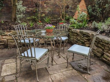 An outdoor patio with a glass table and four metal chairs surrounded by stone walls and plants at The Old Sorting Office in Hawarden
