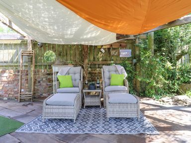 An outdoor seating area with two wicker chairs with footrests and green pillows under shade sails at Sunset Cottage in Swimbridge near Barnstaple