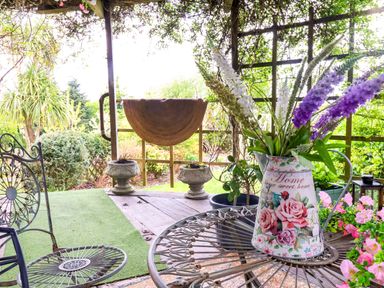 A garden with a table and flowers in a pitcher at Sunset Cottage in Swimbridge near Barnstaple