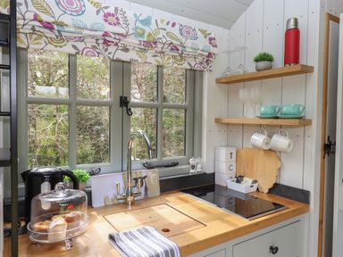 A kitchen sink area with a window and patterned valance above at Burr 1 Shepherds Hut in Barnstaple
