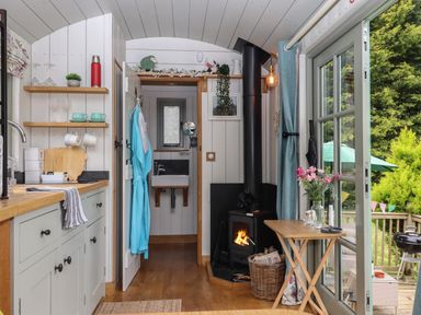 A small kitchen with a sink and shelves next to a wood stove and a folding table with flowers and candles at Burr 1 Shepherds Hut in Barnstaple