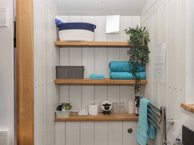 Three wooden shelves with towels baskets a mirror a plant glasses and toiletries in a bathroom at Burr 1 Shepherds Hut in Barnstaple