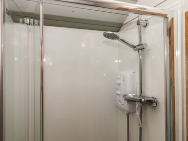 A shower area with a chrome showerhead and a white electric shower unit at Burr 1 Shepherds Hut in Barnstaple