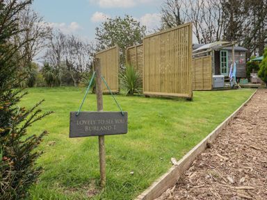 A garden area with a wooden sign that says lovely to see you burland 1 and a wooden hut with partitions at Burr 1 Shepherds Hut in Barnstaple