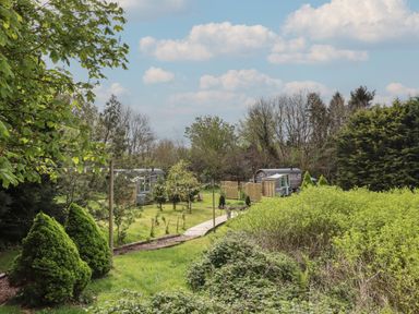 A garden path leading to two shepherds huts surrounded by trees and shrubs at Burr 1 Shepherds Hut in Barnstaple