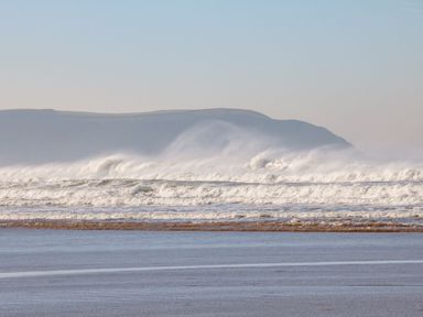 A beach scene with waves crashing and hills in the background at Burr 1 Shepherds Hut in Barnstaple