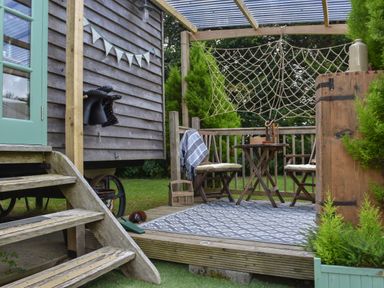 An outdoor wooden deck with two chairs and a table under a pergola with netting at Burr 1 Shepherds Hut in Barnstaple