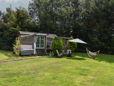 A garden with two wooden chairs and umbrella near a wooden hut on grass at Burr 1 Shepherds Hut in Barnstaple