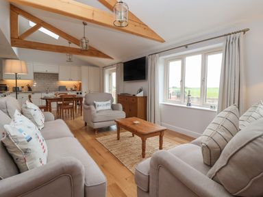 A living room with beige sofas and wooden coffee table next to a dining area with a wooden table and chairs at Waverley Cottage Kilnsea near Easington Hull