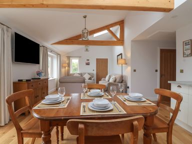 A dining table set with plates and glasses in a room with wooden beams sofas and a television at Waverley Cottage Kilnsea near Easington Hull