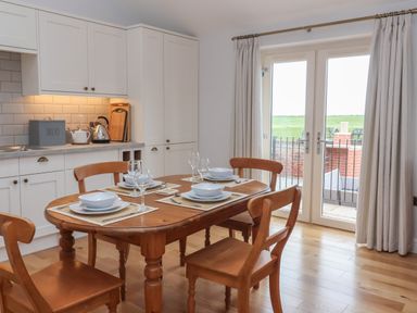 A kitchen with wooden dining table and chairs set with plates and glasses near glass doors at Waverley Cottage Kilnsea near Easington Hull