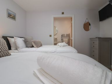 A bedroom with two beds a dresser a wall-mounted TV and an en suite bathroom at Waverley Cottage in Kilnsea near Easington Hull