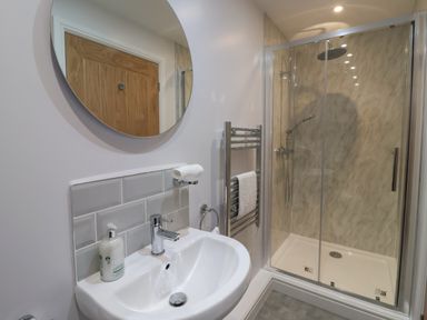 A bathroom with a sink and round mirror next to a glass enclosed shower at Waverley Cottage in Kilnsea near Easington Hull