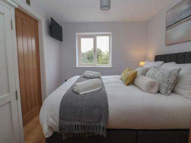 A bedroom with a bed, pillows, rolled towels, a window, a wall-mounted TV, and a wooden door at Waverley Cottage in Kilnsea near Easington Hull