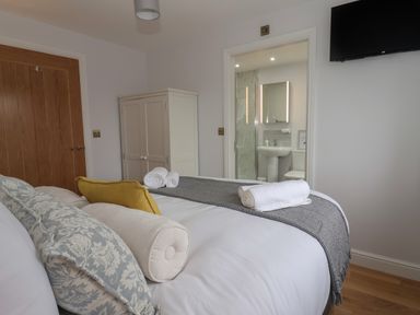 A bedroom with a bed with cushions and towels next to a white wardrobe and an ensuite bathroom at Waverley Cottage in Kilnsea near Easington Hull