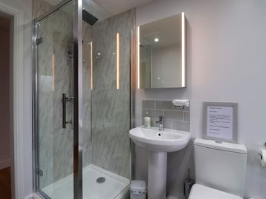 A bathroom with a glass shower enclosure a pedestal sink with a mirror light above and a toilet with a framed notice on the wall at Waverley Cottage Kilnsea near Easington Hull