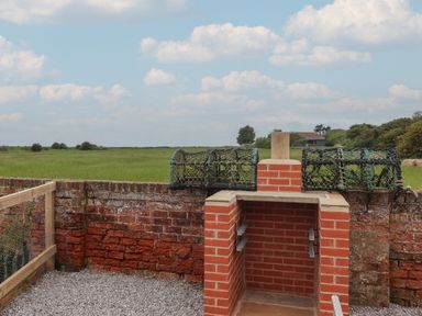 A brick barbecue grill with fishing pots on a brick wall and fields in the background at Waverley Cottage Kilnsea near Easington Hull