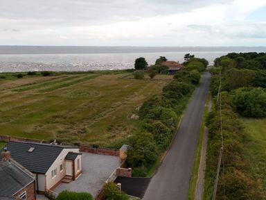 A coastal road with houses bushes and grass fields near the sea at Waverley Cottage Kilnsea near Easington Hull
