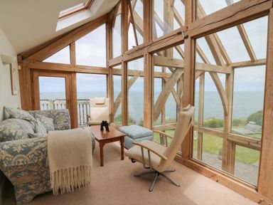 A sitting area with patterned sofa cream armchairs wooden table and large windows overlooking the sea at Pen y Graig in Aberporth
