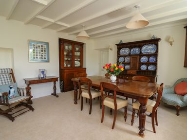 A dining room with a wooden table and chairs a cabinet with blue and white plates and a rocking chair at Pen y Graig in Aberporth