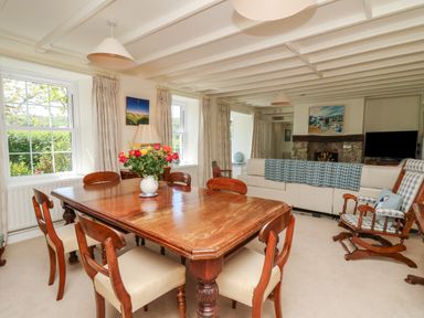A dining area with a wooden table and chairs a vase with flowers two windows a sitting area with a sofa an armchair a fireplace and a television at Pen y Graig in Aberporth