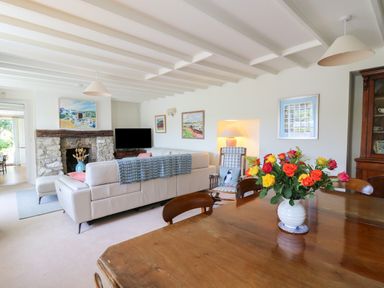A living room with a stone fireplace a white sofa a wooden dining table with flowers and paintings on the walls at Pen y Graig in Aberporth