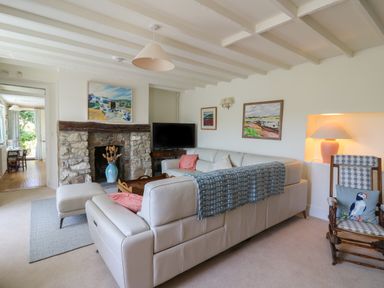 A living room with a stone fireplace a white leather sofa a wooden rocking chair and paintings on the walls at Pen y Graig in Aberporth