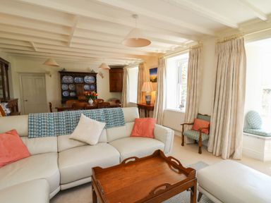A living room with a white sofa and wooden coffee table beside a dining table with a wooden dresser in the background at Pen y Graig in Aberporth