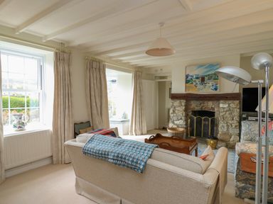 A living room with a stone fireplace sofa armchairs floor lamps and windows with curtains at Pen y Graig in Aberporth