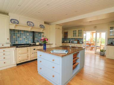 A kitchen with a large blue island and stone countertop a stove with blue tile backsplash and a dining area visible through glass doors at Pen y Graig in Aberporth