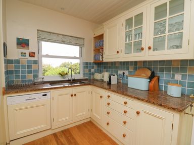 A kitchen with cream cabinets blue tiled backsplash and a window above the sink at Pen y Graig in Aberporth