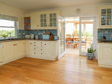 A kitchen with wooden floor white cabinets blue tiled backsplash and a door opening to a dining area at Pen y Graig in Aberporth