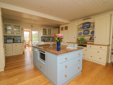 A kitchen with a blue island with a granite countertop and flowers in a blue vase at Pen y Graig in Aberporth
